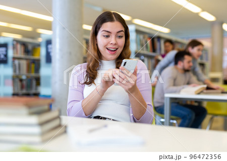 Woman typing a message on the phone in the public library Woman typing a message on the phone in the public library 96472356