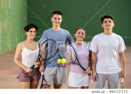 Happy frontenis players with rackets and balls standing in open court Happy frontenis players with rackets and balls standing in open court 96472373