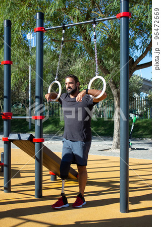 Young man with leg prothesis using gymnastic rings for training 96472669