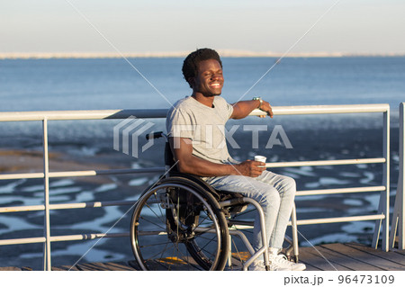 Young man in wheelchair enjoying takeaway espresso at seafront Young man in wheelchair enjoying takeaway espresso at seafront 96473109