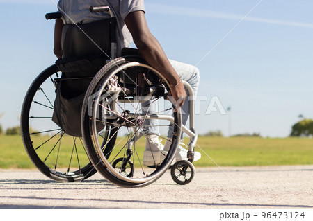 Black man in wheelchair riding along park road 96473124