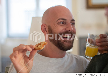 Happy gay eating biscuit and drinking juice in bed in morning Happy gay eating biscuit and drinking juice in bed in morning 96473125