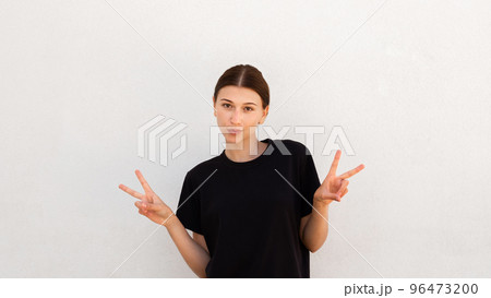 Portrait of confident young woman making victory gesture 96473200