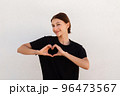 Portrait of positive young woman making heart gesture 96473567