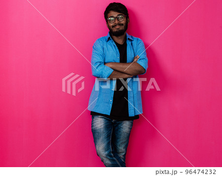 Indian smiling young student in blue shirt and glasses posing on pink background Indian smiling young student in blue shirt and glasses posing on pink background 96474232