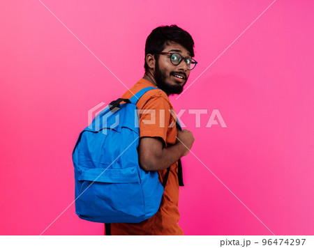 Indian student with blue backpack, glasses and notebook posing on pink background. The concept of education and schooling. Time to go back to school Indian student with blue backpack, glasses and notebook posing on pink background. The concept of education and schooling. Time to go back to school 96474297