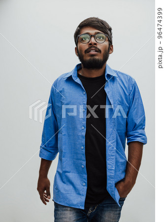 Indian smiling young man with blue shirt and glasses posing on gray background Indian smiling young man with blue shirt and glasses posing on gray background 96474399