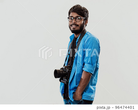 Professional photographer having DSLR camera taking picture.Indian man photography enthusiast taking photo while standing on blue background. Studio shot 96474401