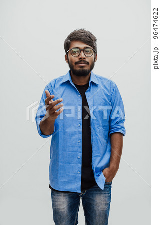 Indian smiling young man with blue shirt and glasses posing on gray background Indian smiling young man with blue shirt and glasses posing on gray background 96474622
