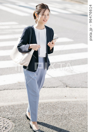 スマホを持ちながら歩く働く女性 96476614