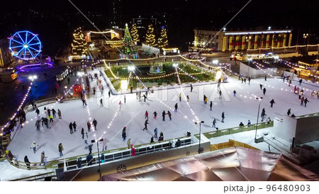 Many people skating on beautiful ice skating rink in open air decorated New Year Christmas illuminations, decorations, luminous garlands on winter night. New Year Christmas holiday celebration. Aerial 96480903