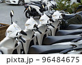 Motorcycles for rent or for sale on the city street. Lots of white scooters to ride. 96484675