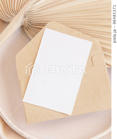 Card and envelope on plate on dried palm leaf and beige silky fabric close up, greeting or wedding mockup 96485371