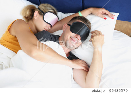 Couple in sleeping masks in bed together embracing 96486579