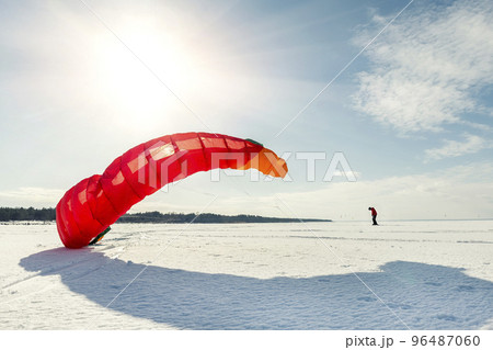 Panoramic view of many people friends enjoy riding kite surf board in warm suit on bright sunny winter day at frozen lake field snowy surface. Wintersport adrenaline fun adventure hobby acitivity 96487060