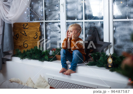 boy in a sweater sits on windowsill at home, waiting for miracles, gifts and Christmas 96487587