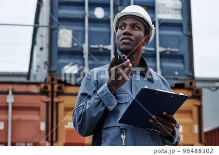 Male worker wearing hardhat and talking to radio in shipping docks Male worker wearing hardhat and talking to radio in shipping docks 96488302