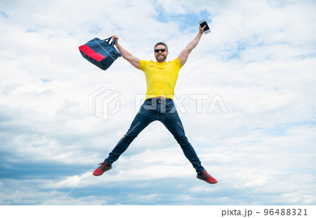 Active man jumping with travel bag midair sky background, vacation 96488321