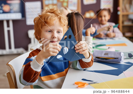 Cute primary school learner holding blue paper with holes for eyes and mouth Cute primary school learner holding blue paper with holes for eyes and mouth 96488644