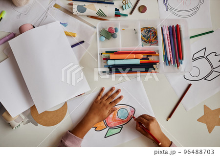 Above view of hands of little African American learner drawing rocket Above view of hands of little African American learner drawing rocket 96488703