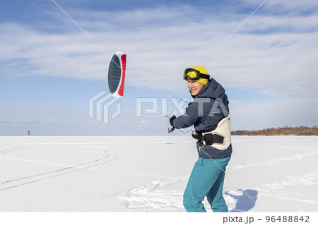 Panoramic view of many people friends enjoy riding kite surf board in warm suit on bright sunny winter day at frozen lake field snowy surface. Wintersport adrenaline fun adventure hobby acitivity 96488842