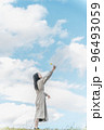 広大な青空のもとで手を伸ばすロングヘアーの女性 96493059