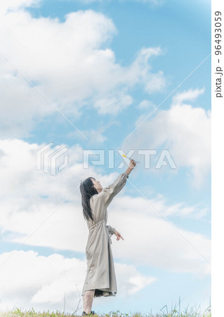 広大な青空のもとで手を伸ばすロングヘアーの女性 96493059