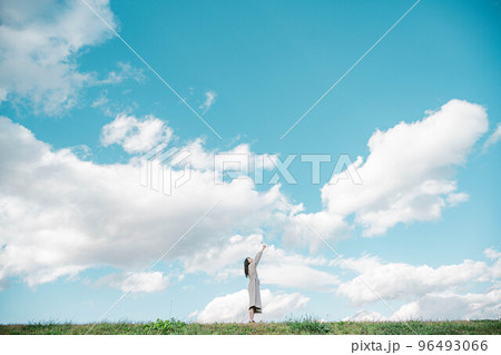 広大な青空のもとで手を伸ばすロングヘアーの女性 96493066