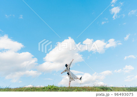 広大な青空のもとで手を伸ばすロングヘアーの女性 96493075