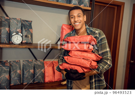 Joyful worker standing in a storeroom beside shelves with goods Joyful worker standing in a storeroom beside shelves with goods 96493523