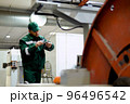 factory worker in a robe and cap checks the performance of the device for the production of cable products from a copper core 96496542