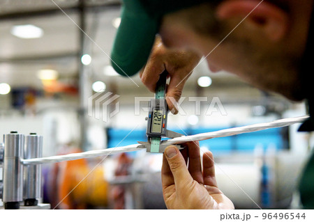 factory worker in a robe and cap checks the performance of the device for the production of cable products from a copper core 96496544