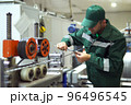 factory worker in a robe and cap checks the performance of the device for the production of cable products from a copper core 96496545