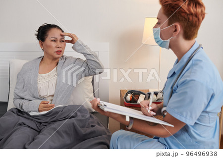 Senior woman complaining about headache to doctor visiting her at home Senior woman complaining about headache to doctor visiting her at home 96496938