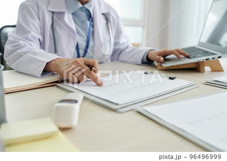 Cropped image of cardiologist checking cardiogram of patient Cropped image of cardiologist checking cardiogram of patient 96496999