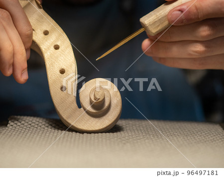 luthier artisan maker sculpting and carving violin scroll and neck with chisel 96497181