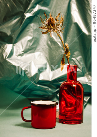 Red glass vase and scarlet cup of tea standing on table on green mint background. Vertical still life with dishes, decor for a stylish home. Hygge style at modern home. Dark backdrop for mobile phone. Red glass vase and scarlet cup of tea standing on table on green mint background. Vertical still life with dishes, decor for a stylish home. Hygge style at modern home. Dark backdrop for mobile phone. 96497247