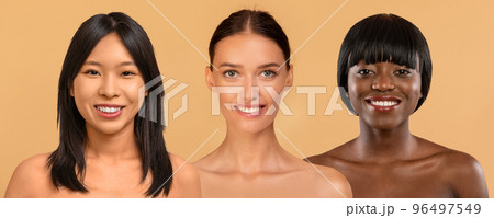 Beautiful multicultural half-naked young ladies smiling at camera on beige Beautiful multicultural half-naked young ladies smiling at camera on beige 96497549