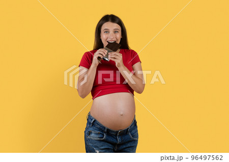 Pregnancy Cravings. Happy Young Pregnant Woman Biting Chocolate Bar 96497562