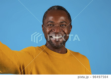 Closeup of happy handsome black man taking selfie on blue Closeup of happy handsome black man taking selfie on blue 96497564