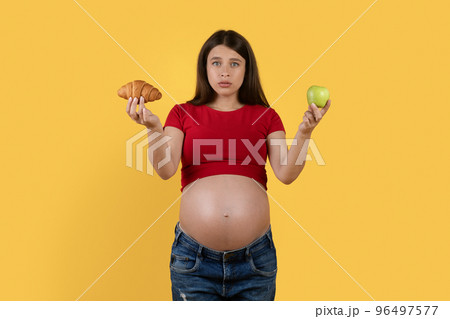 Confused Pregnant Woman Holding Croissant And Green Apple In Hands 96497577