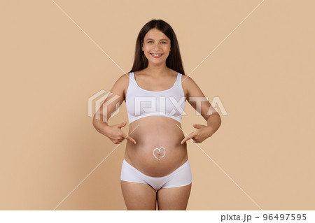 Happy Pregnant Female Pointing At Heart Shape Made Of Cream On Belly 96497595