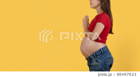 Cropped Shot Of Pregnant Woman Standing With Clasped Hands Over Yellow Background 96497633