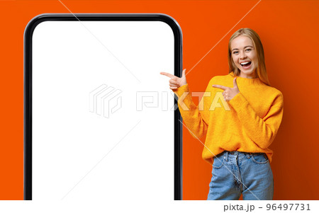 Check This. Cheerful Teen Girl Pointing At Big Cellphone With Blank Screen 96497731
