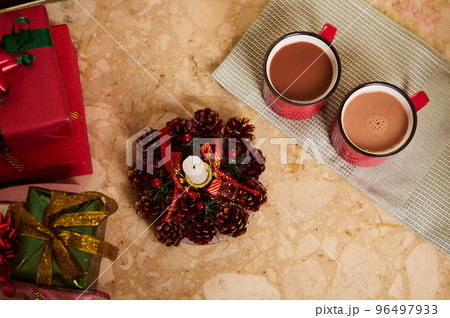 View from above of two red cups with hot cocoa or chocolate drink on a green napkin, next to a decorative Christmas lit candle and beautiful presents on marble table. New Year atmosphere at home. 96497933