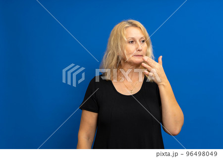 Photo of thoughtful contemplative woman pursing lips with mysterious expression, looking puzzled to side, dressed in t-shirt, isolated over blue background with free copy space. Photo of thoughtful contemplative woman pursing lips with mysterious expression, looking puzzled to side, dressed in t-shirt, isolated over blue background with free copy space. 96498049