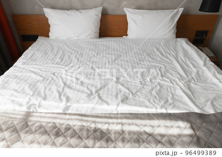 Wide empty bed with wooden headboard two white pillows 96499389