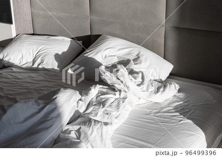Crumpled empty bed with blanket and pillows 96499396