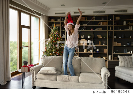Happy young woman in festive mood jumping on couch. Happy young woman in festive mood jumping on couch. 96499548