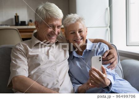 Senior couple using modern smartphone seated on sofa at home 96499706